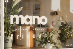 Schaufenster des Friseursalons mano in Weinheim mit Logo und Pflanzen